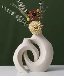 Two modern, cream-colored vases with abstract curved shapes holding dried flowers, set against a dark green background. | 28Alchemy