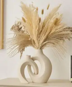 Modern beige ceramic vase with intertwined loops holding dried pampas grass, placed on a light-colored surface. | 28Alchemy