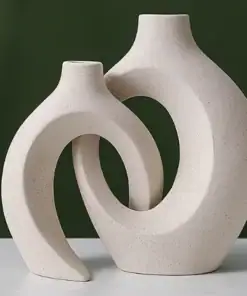 Two modern, abstract ceramic vases with curved, open designs sit on a white surface against a dark green background. | 28Alchemy