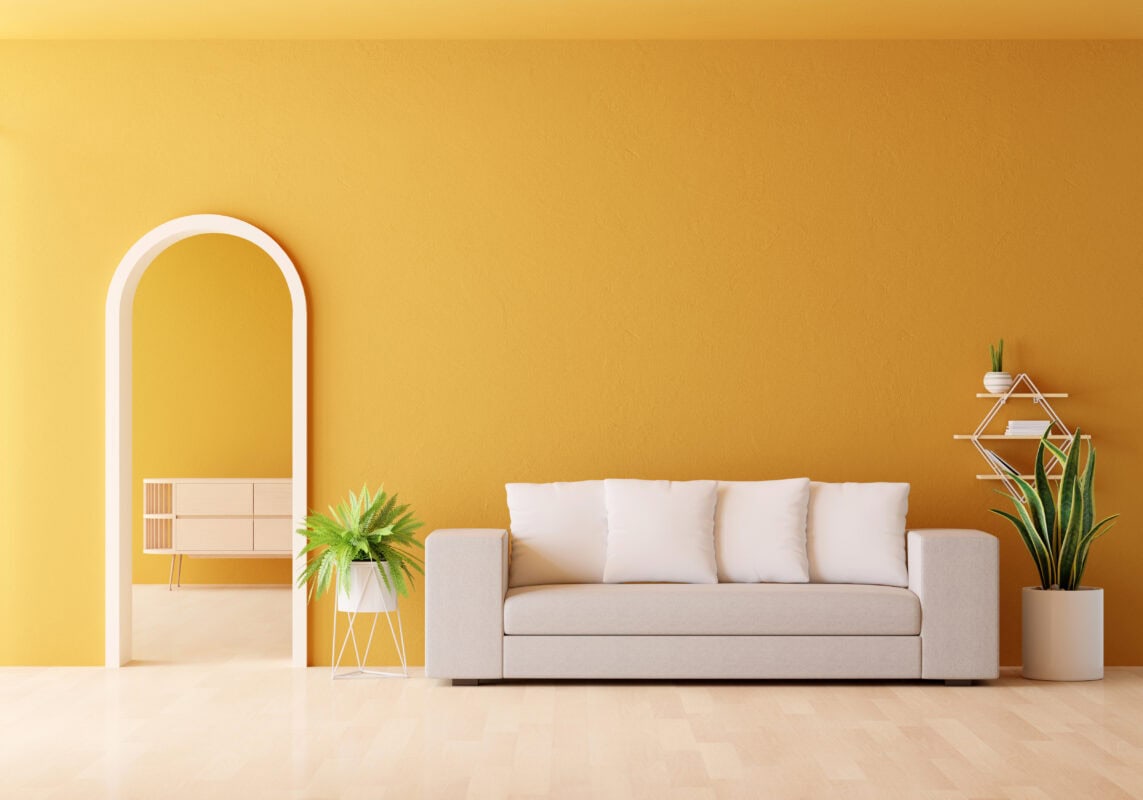 Modern living room with a beige sofa, white pillows, green plants, and yellow walls featuring an arched doorway. | 28Alchemy
