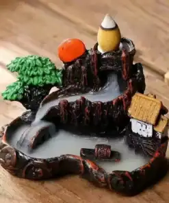 Miniature incense waterfall with tree, house, and mist flowing down rocky steps on a wooden surface. | 28Alchemy