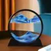 A round glass sand art frame with blue and white sand forming mountain-like patterns, placed on a table. | 28Alchemy