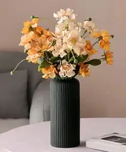 A black ribbed vase with orange and cream flowers on a light pink table, with a sofa in the background. | 28Alchemy