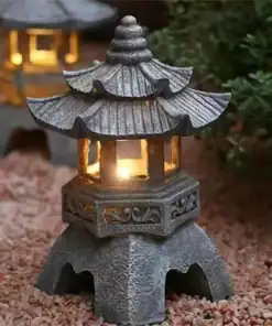 A small stone lantern with a lit candle inside sits on gravel, with another lantern glowing in the background. | 28Alchemy