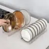 Two metal racks holding pot lids and white plates on a kitchen counter, with a hand reaching for a lid. | 28Alchemy