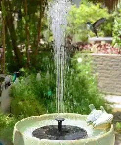 Two hummingbirds hover near a birdbath fountain with water spraying upward in a lush garden setting. | 28Alchemy