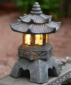A small stone lantern with a pagoda-style roof, glowing warmly, set on a decorative outdoor surface. | 28Alchemy