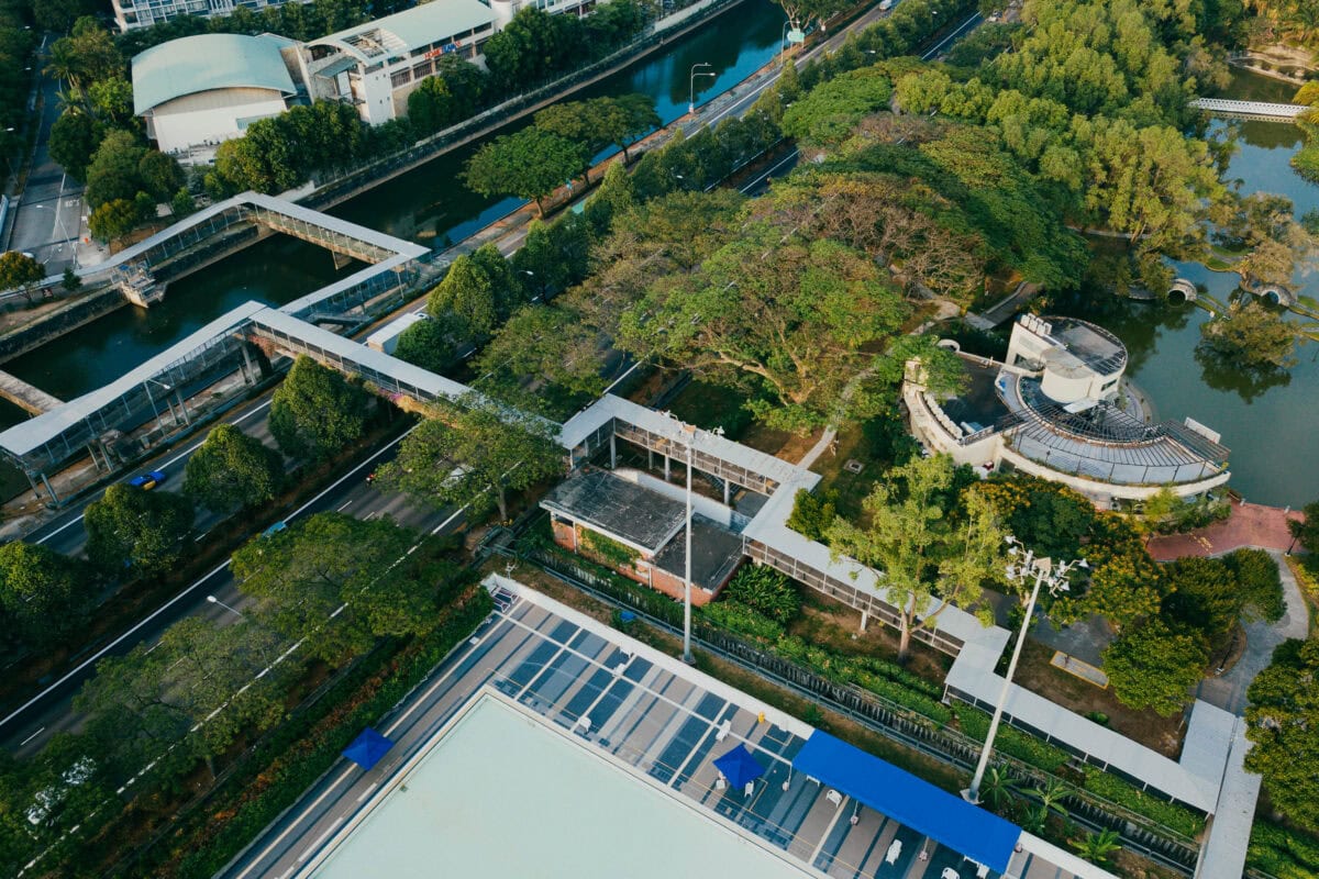 Aerial view of a park with trees, walkways, water features, and nearby buildings surrounded by roads. | 28Alchemy