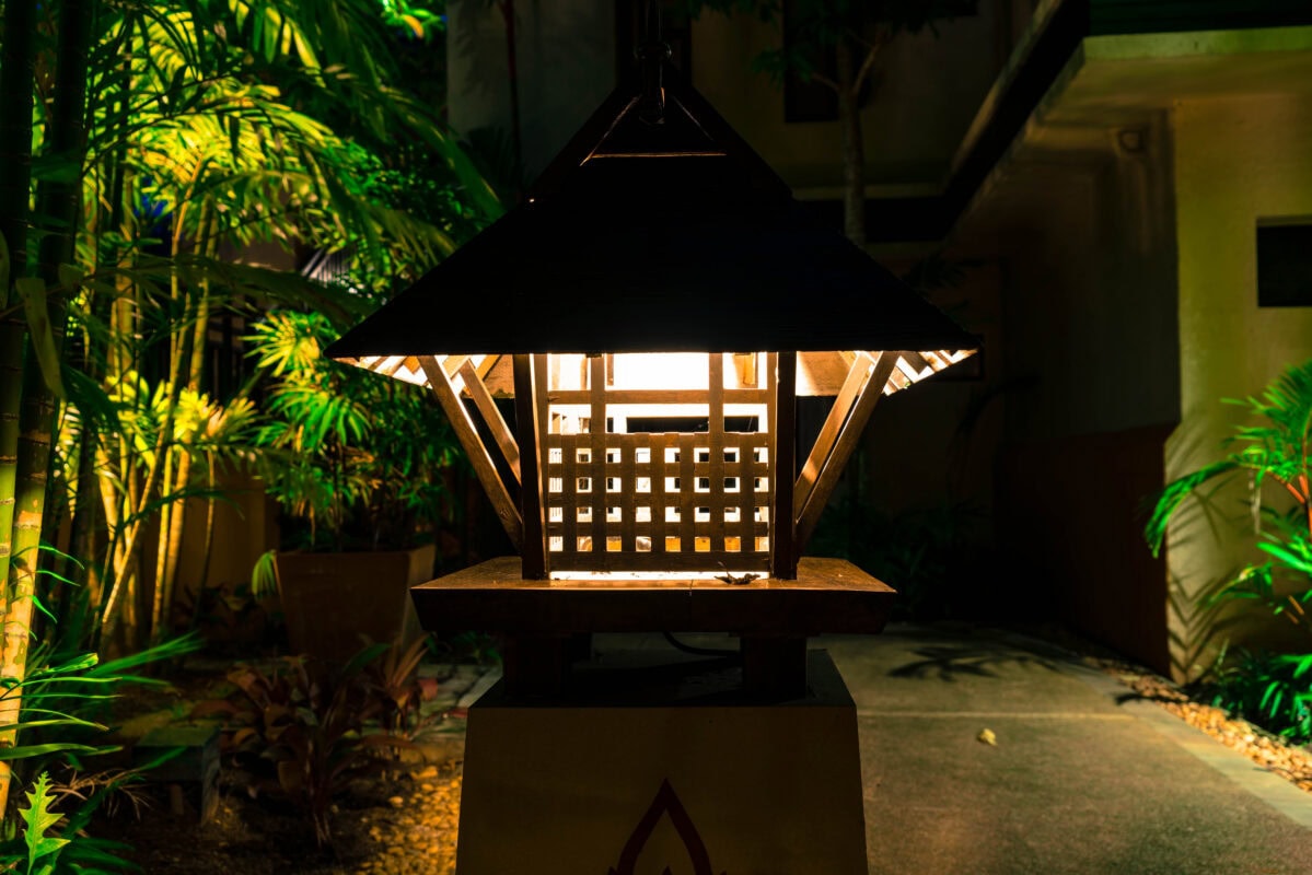 A glowing lantern with a lattice design illuminates a garden path surrounded by lush green plants at night. | 28Alchemy