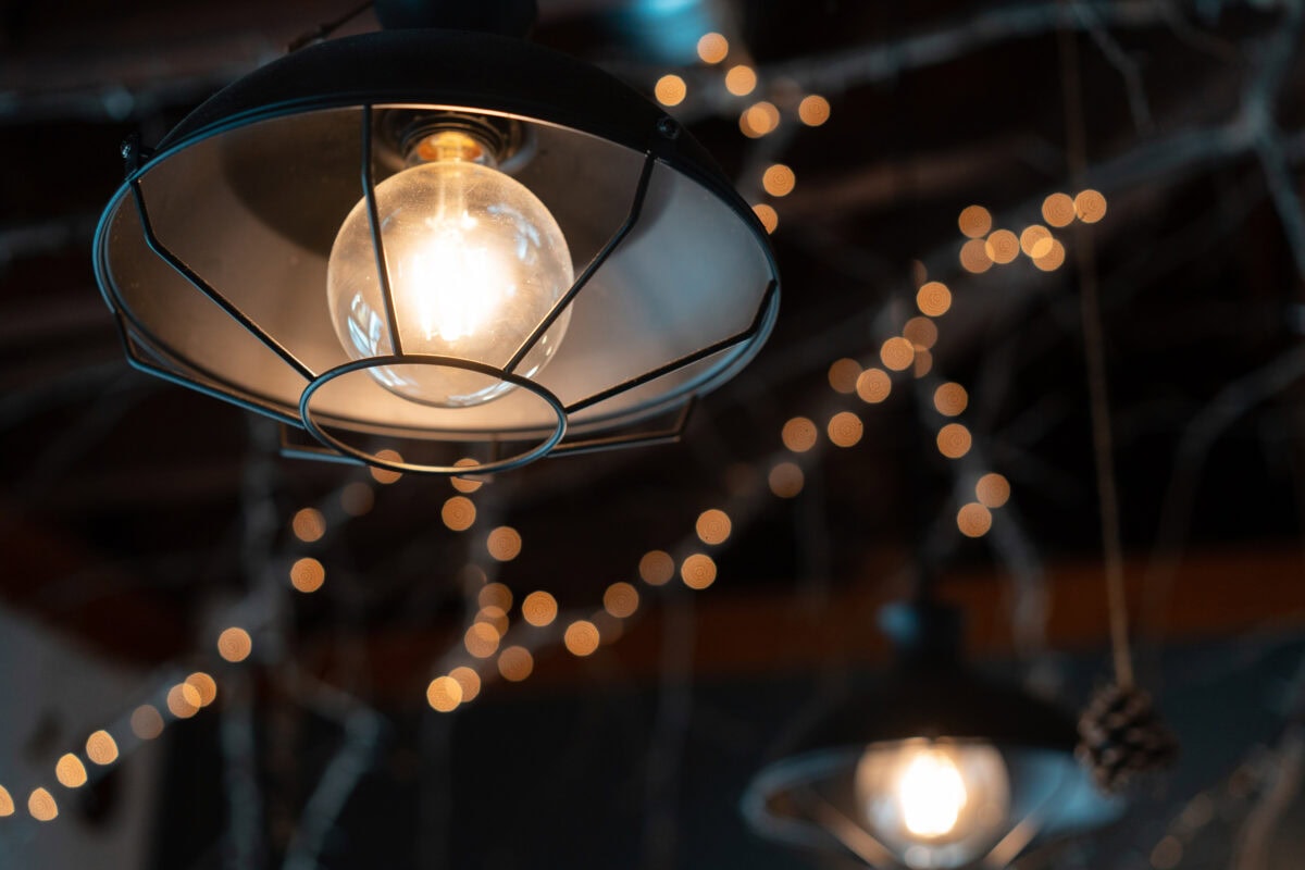 A close-up of a hanging light bulb with string lights blurred in the background. | 28Alchemy