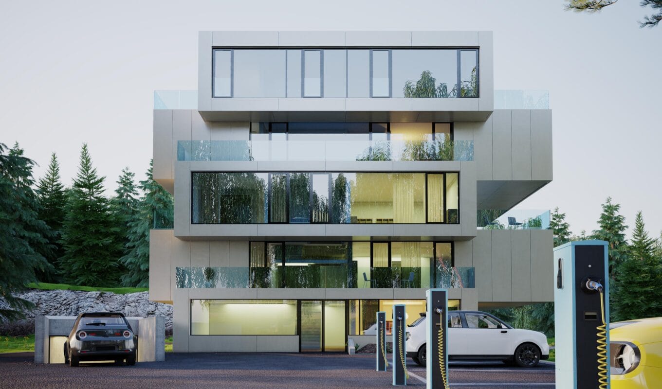 Modern three-story building with glass balconies, parked electric cars, and EV charging stations in front, surrounded by trees. | 28Alchemy