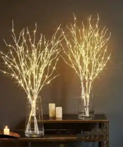 Two glass vases hold lit decorative birch branches next to lit candles on a dark table and against a dark wall. | 28Alchemy