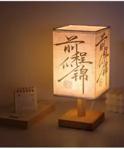 A square table lamp with Chinese calligraphy, glowing warmly on a desk beside a small calendar and a decorative object. | 28Alchemy