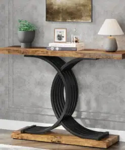 Wood console table with a black curved base, topped with books, a plant, a lamp, and a framed photo against a gray wall. | 28Alchemy