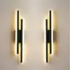 Two modern wall sconces with vertical black bars and glowing white light strips, mounted on a light-colored wall. | 28Alchemy