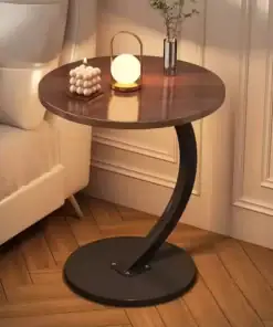 Round wooden side table with a modern black curved base, holding a candle, glowing lamp, and small plant. | 28Alchemy