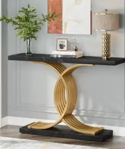 A modern console table with a black top, gold curved base, lamp, plant, and decor items against a gray paneled wall. | 28Alchemy