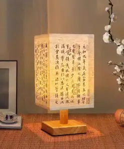 A lit table lamp with a shade displaying Chinese calligraphy, beside a teacup and blooming white flowers. | 28Alchemy
