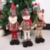 Three plush Christmas dolls—a Santa, a snowman, and a reindeer—stand in front of a decorated Christmas tree. | 28Alchemy