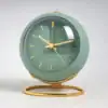 Green round quartz clock with gold hands and stand, showing the time as 9:08, against a light background. | 28Alchemy
