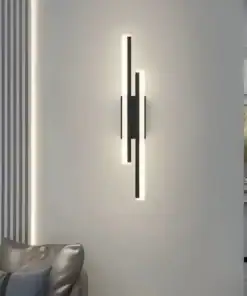Modern vertical wall sconce with black and white geometric lines glowing on a light gray wall above a silver chair. | 28Alchemy