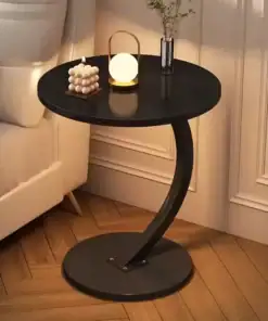 Round black side table with curved base, placed by a sofa, decorated with a candle, lamp, and small vase. | 28Alchemy