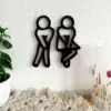 Black restroom symbols of a man and a woman with crossed legs, mounted on a white wall near plants and a candle. | 28Alchemy