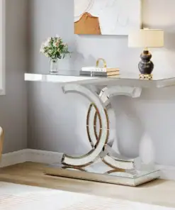 A mirrored console table with a decorative base, topped with flowers, a book, and a lamp in a bright living room. | 28Alchemy