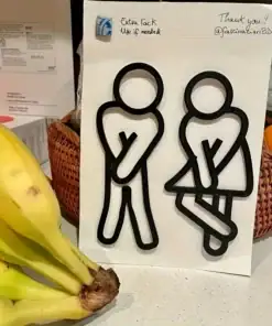 Two black restroom symbols look desperate to go, standing on a counter near bananas and a woven basket. | 28Alchemy