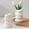 Two white, spiral-shaped vases; one holds two white tulips, both placed on a light wooden tray. | 28Alchemy