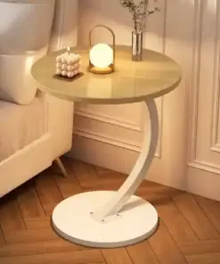Round wooden side table with a modern curved base, holding a candle, a small lamp, and a vase with flowers. | 28Alchemy