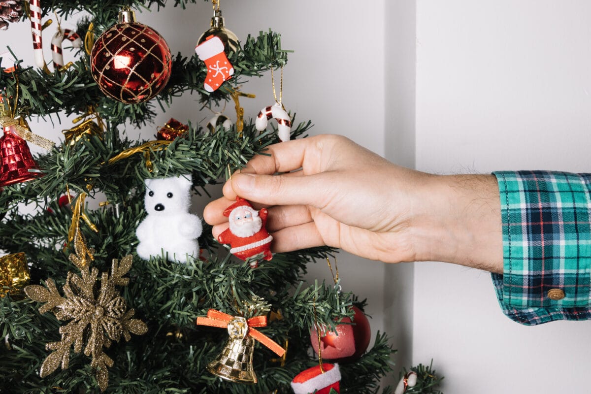 A hand places a small Santa ornament on a decorated Christmas tree with various ornaments. | 28Alchemy