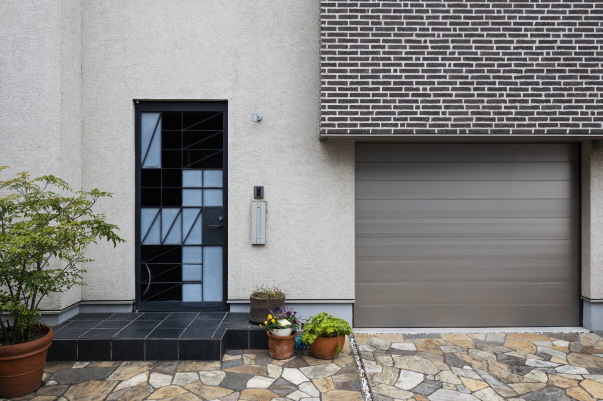 Modern house exterior with a black geometric front door, gray garage door, potted plants, and stone pathway. | 28Alchemy