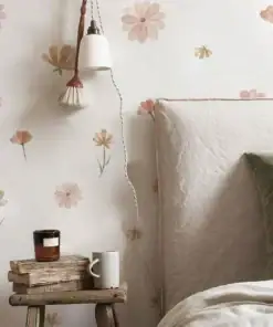 Cozy bedroom corner with floral wallpaper, a lamp, a stool holding a candle and mug, and a bed with beige and green pillows. | 28Alchemy