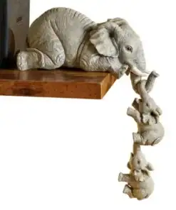 Sculpture of three small elephants hanging down from a bookshelf, each holding the other's tail with its trunk. | 28Alchemy
