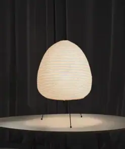 A glowing paper lantern lamp with tripod legs on a round table, set against dark curtains. | 28Alchemy