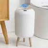 A white smart trash can with wooden legs and a blue Wi-Fi symbol above it, placed in a modern bathroom. | 28Alchemy