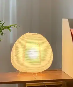 A round paper lantern lamp glows on a wooden table beside a potted plant and books. | 28Alchemy