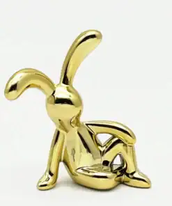 A shiny gold sculpture of a relaxed, cartoon-like rabbit sitting with one arm resting on its raised knee. | 28Alchemy