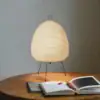 A glowing paper lantern lamp on a wooden table beside an open book and red pen. | 28Alchemy