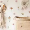 A nursery with floral wall decals, a woven basket on a wooden dresser, and hanging blankets on hooks. | 28Alchemy