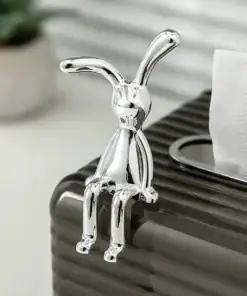 A shiny silver bunny figurine sits on the edge of a dark tissue box with tissues sticking out. | 28Alchemy
