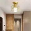 Modern ceiling light with a geometric gold frame and white bulb, installed in a hallway with wood and beige walls. | 28Alchemy