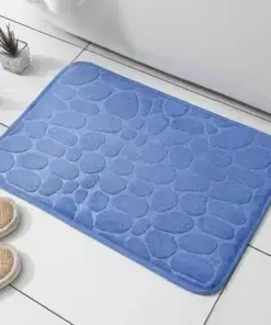 A blue, pebble-patterned bath mat on white tile floor next to beige slippers and a black wire basket with a plant. | 28Alchemy