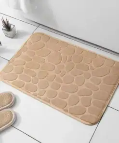 Beige, pebble-patterned bath mat on white tiled floor with slippers and a small plant nearby. | 28Alchemy