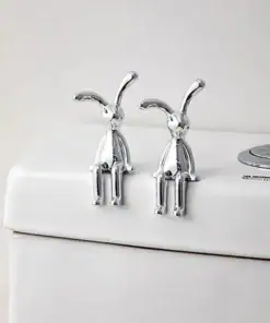 Two silver rabbit figurines sit on the edge of a white toilet tank in a minimal bathroom setting. | 28Alchemy