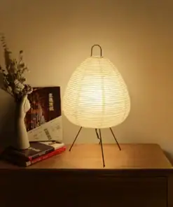 A glowing paper lantern lamp on a wooden nightstand beside a vase with dried flowers and some books. | 28Alchemy