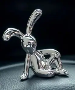 A shiny silver sculpture of a relaxed, abstract bunny sits on a textured black surface. | 28Alchemy