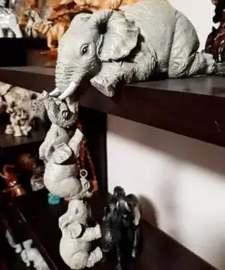 Three elephant figurines hang off a shelf, each holding the next with their trunks, forming a playful chain. | 28Alchemy