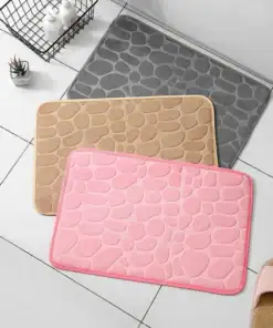 Three textured bath mats in pink, beige, and gray are laid on a white tiled floor near slippers and toiletries. | 28Alchemy